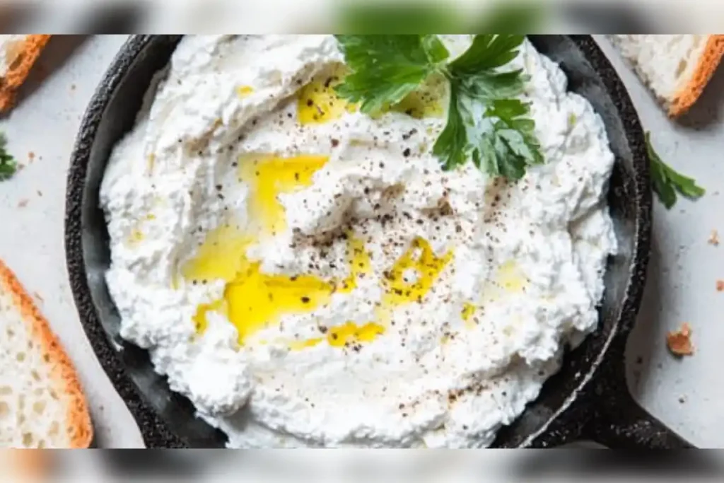 Ricotta cheese drizzled with olive oil and garnished with fresh herbs in a skillet, ready to be served with crusty bread.